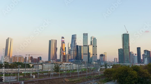 Sunset timelapse of Moscow City towers with railroad and moving train in the foreground