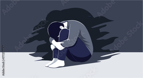 A person sits alone, embracing their knees amidst a shadowy backdrop, conveying feelings of sadness, isolation, and emotional distress.