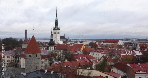 Wallpaper Mural Panoramic view over Tallinn Old Town: a medieval stone tower, red roofs, and the sharp spire of St. Olaf's Church rising above the city, with the Baltic Sea on the horizon under soft autumn clouds. Torontodigital.ca