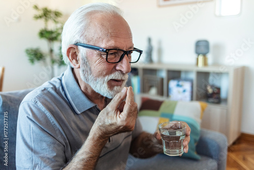 Vászonkép Senior man takes pill with glass of water in hand