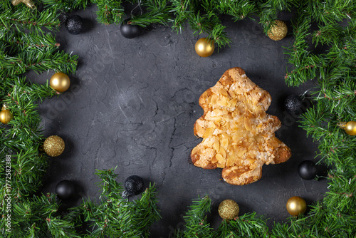 Festive christmas tree pastry with almonds surrounded by pine and baubles on dark stone background