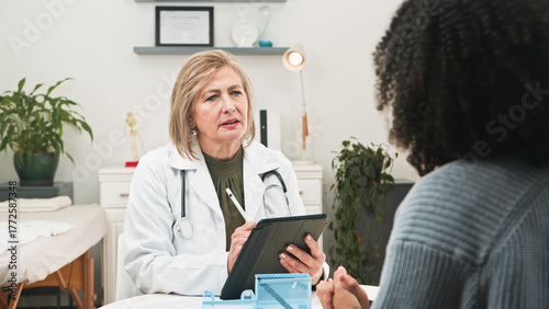Female Doctor Consulting With Patient In Clinic Using Tablet During Medical Appointment