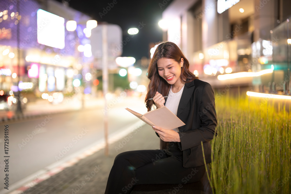 Fototapeta premium Asian businesswoman smiling reading notebook at night city