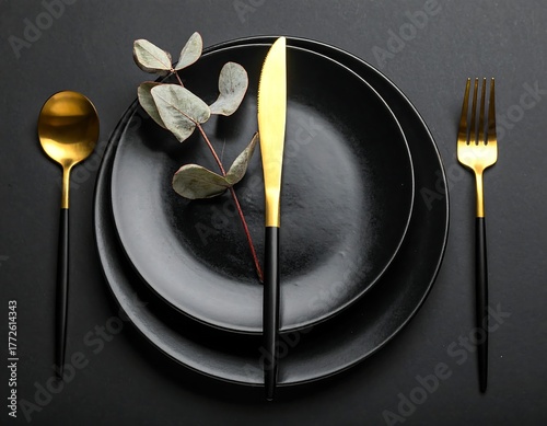 Overhead view of a formal table setting with black plates and gold cutlery