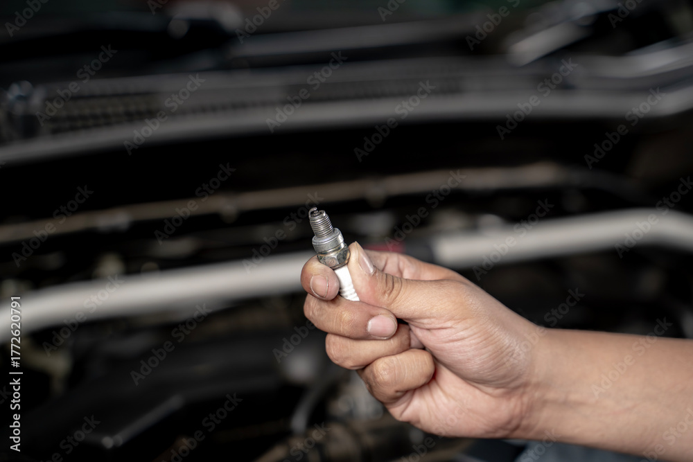 Fototapeta premium Close-up of a man’s hand holding a car spark plug, representing automotive maintenance, mechanic work, vehicle repair, and engineering technology.