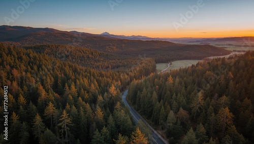 Aerial view of a mountain road surrounded by woods at sunset, showcasing seasonal change