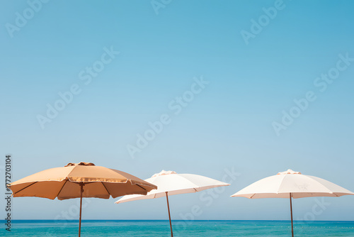 Three beach umbrellas stand against a clear blue sky and turquoise water
