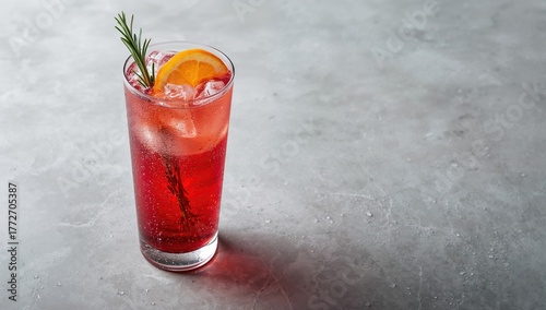 Tall glass of cranberry cocktail garnished with fresh orange on a pale stone surface