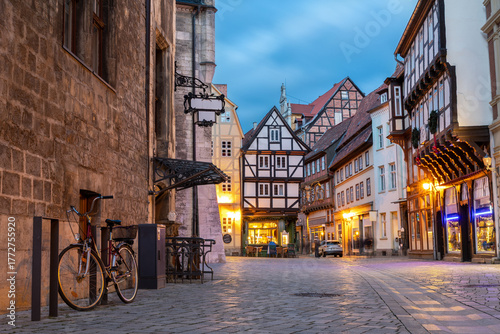 Fototapeta Naklejka Na Ścianę i Meble -  Charming Quedlinburg town evening street view illuminated with lights old St. Nicholas Church St. Nicholas Kirche cafe restaurant  historical half-timbered houses facade. Festive city German