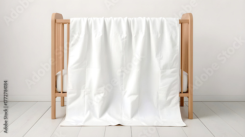 Minimalistic baby crib with soft white blanket hanging over wooden rails, cozy Scandinavian nursery interior, clean neutral background, natural daylight, mockup for baby bedding design