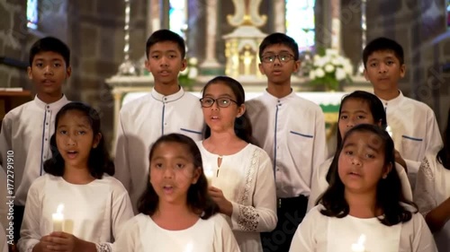 A diverse group of children in white robes sing with candles in a church.