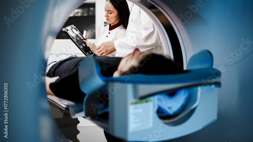 Medical professional analyzing CT scan results while patient lies on examination table inside CT scanner, showcasing advanced imaging technology and diagnostic procedures