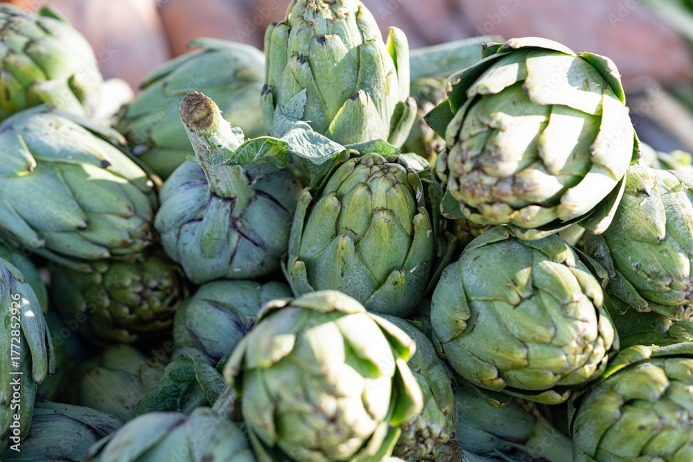 Fototapeta premium Tight cluster of globe artichokes at a farmers’ market; selective focus and bright light showcase fresh produce structure for organic fruits lifestyle and spring recipes.