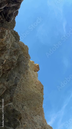 Dramatic rock formations under blue sky, camera pans upward revealing heights