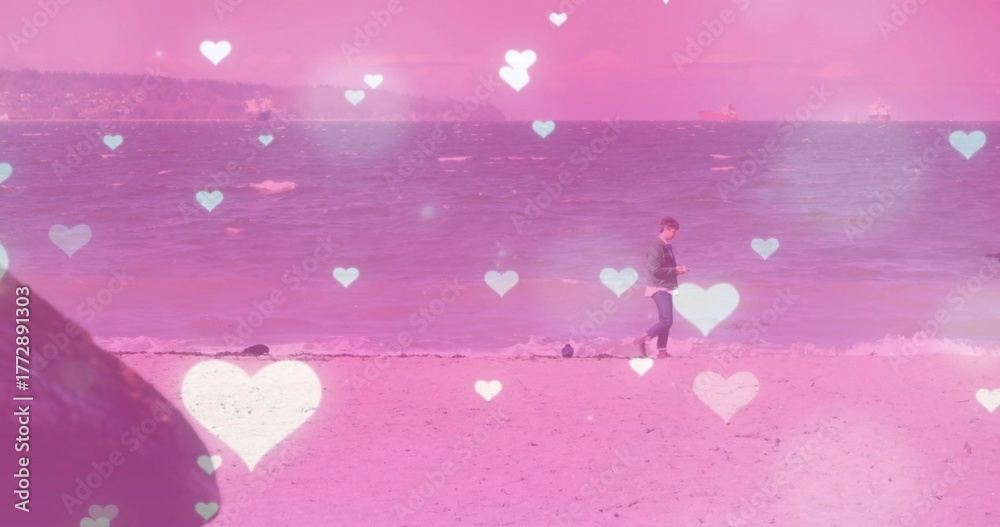 Fototapeta premium Walking man in jacket and jeans along sandy beach water's edge, with smartphone, copy space