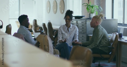 Discussing colleagues in shirts gesturing around laptop in open-plan office, with coffee cup