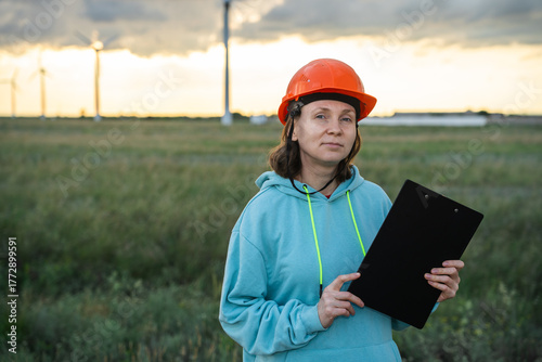 Woman in helmet at a wind farm with clipboard
