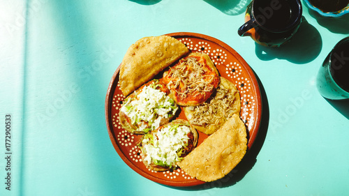 Platillo mexicano con antojitos variados —sopes, tacos dorados y gorditas— servidos en plato de barro sobre una mesa turquesa con luz natural.