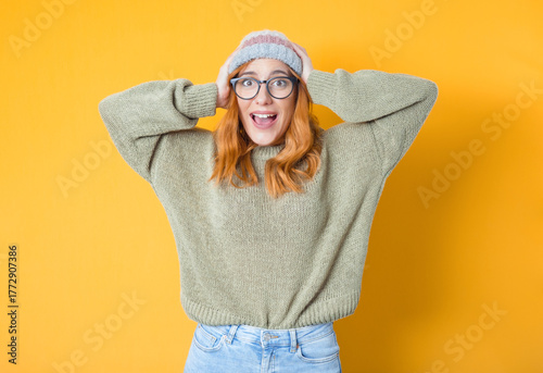 Astonished happy girl with hands on his head, isolated on yellow background. Positive news. Ecstatic pretty woman