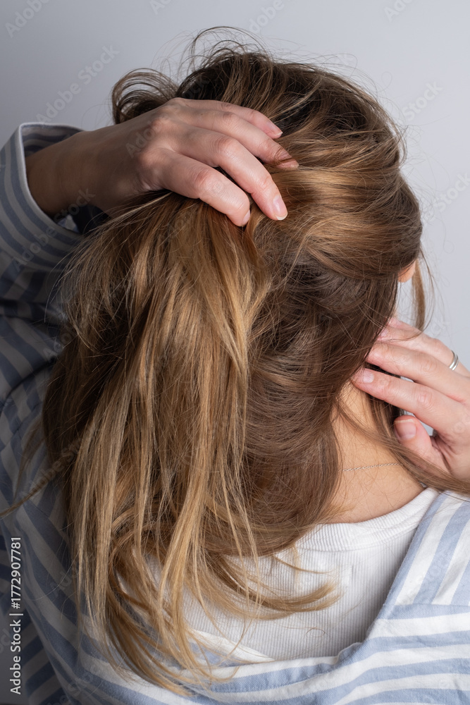 Fototapeta premium Woman combs and styles her long, blond hair. Close-up of a young woman combing her long hair. Concept of self-care, hair health, and self-care at home.
