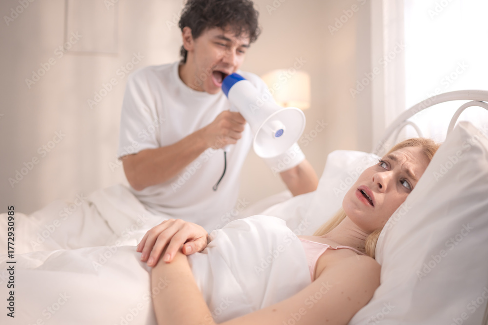Obraz premium Playful man using a megaphone to wake up his partner in the morning