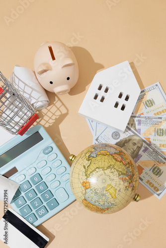 Top down close up view of symbolic economy objects: calculator, wooden house, bills, globe, piggy bank, and receipts representing an economic concept