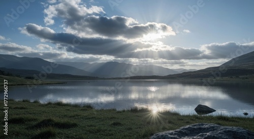 Sunbeams break through clouds over a tranquil lake and distant mountains