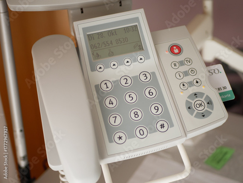 Close-up of modern hospital bedside communication device with numeric keypad, display, and control buttons for patient use in healthcare room. High quality photo