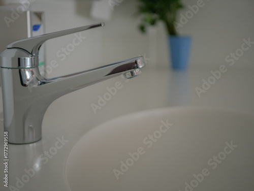 Chrome faucet in a clean hospital bathroom interior with white sink surface and blurred hygiene items in background, modern medical facility. High quality photo