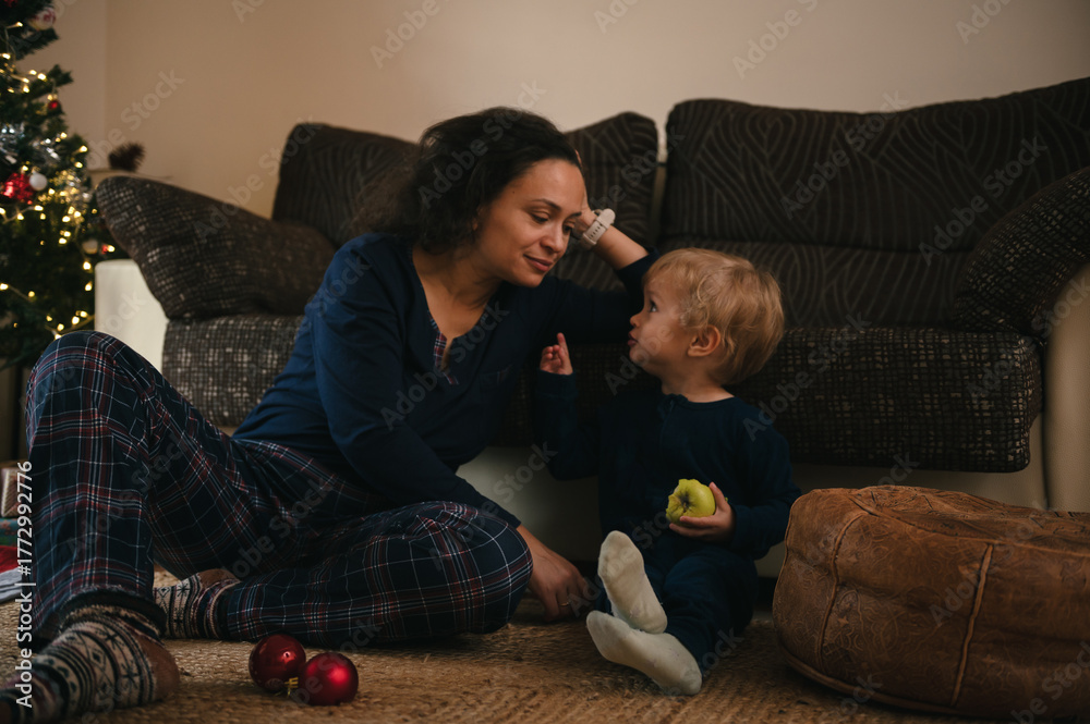 © Taras Grebinets - Mother And Toddler Share Warm Moment On Living Room Carpet By Christmas Tree
