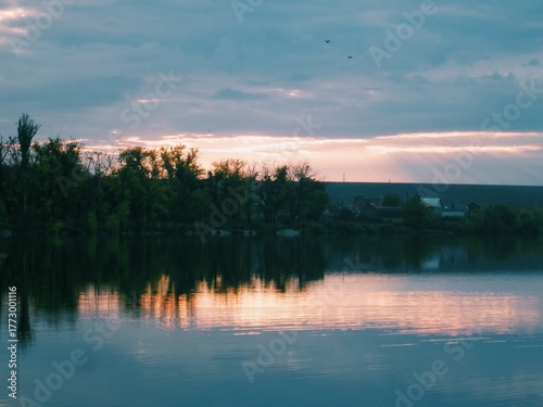 Golden sun rays piercing cloudy sky and reflecting a soft glow on tranquil water surface 