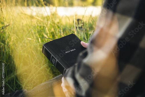 Photography Man is holding the holy Bible in a field during sunset, concept for faith, spirituality, and religion