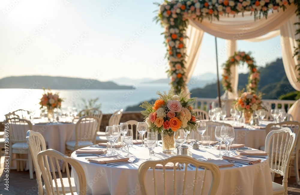 Obraz premium Elegant seaside wedding reception tables set for dinner, adorned with flowers. Scenic ocean backdrop with hazy mountains visible. White chairs await guests.