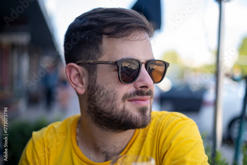 Attractive young man with beard in his 20s wearing sunglasses outside on a sunny day, head turned to the side
