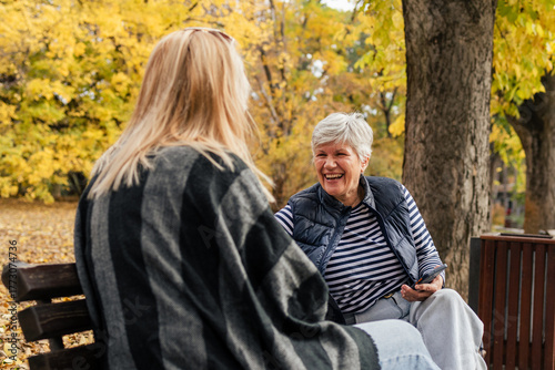Mother and daughter talking in autumn park bench