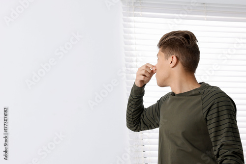 Foto Young man suffering from bad smell and covering his nose indoors, space for text