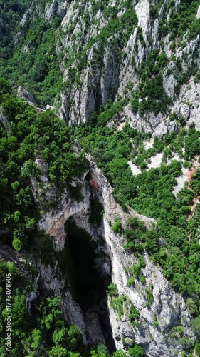 4k vertical aerial view from drone footage showing a dramatic natural rock arch and steep cliffs surrounded by lush green forest in Lazar Canyon, Serbia, during spring