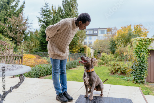 Black woman training pit bull dog in autumn backyard