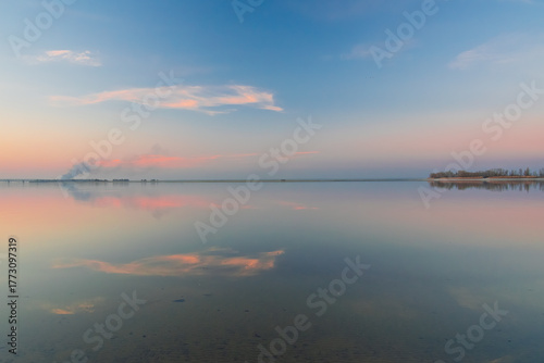 Still lake water perfectly reflecting the soft pastel colors of a tranquil sky at sunset, creating a peaceful and serene natural landscape with a clear horizon line