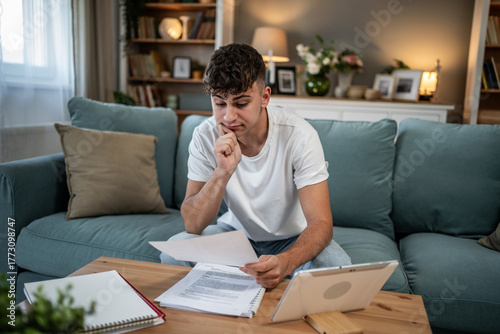 Young man feeling financial stress studying bills at home