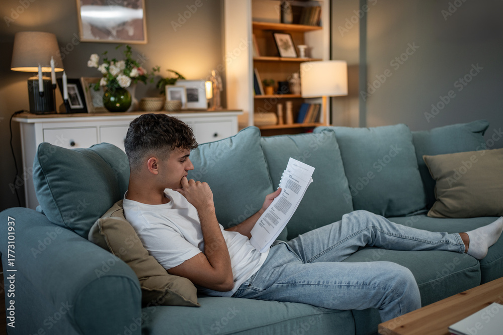 Obraz premium Young man studying documents reading on living room couch