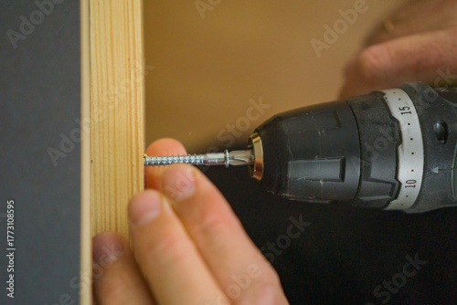 Bild auf Leinwand hands using a cordless electric drill to drive a long silver screw into a wooden