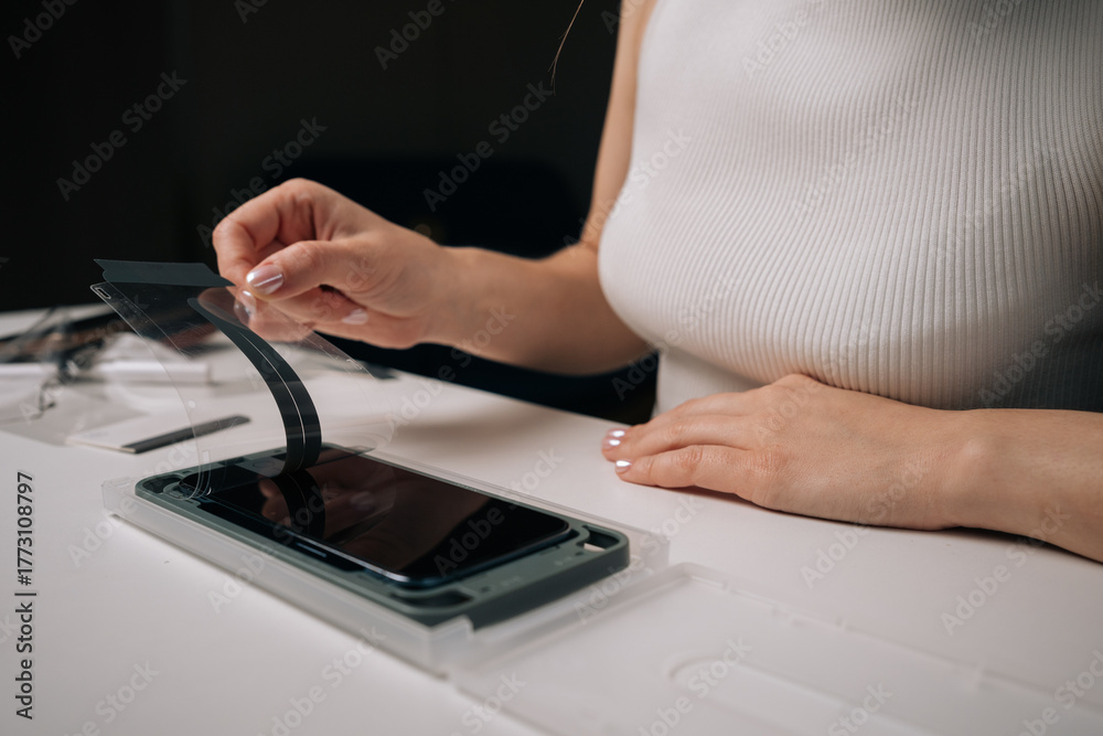 Fototapeta premium Cropped shot of woman installing screen protector on smartphone using specialized machine, ensuring perfect alignment and protection against scratches. Concept of mobile phone maintenance