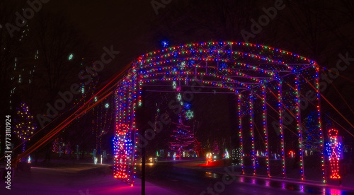 A brightly lit sleigh and reindeer points to a lighted car tunnel entryway to a city park Christmas display.