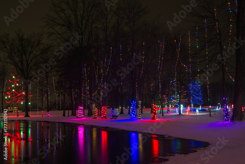 Festive Christmas lighting in a northeast Ohio city park is reflected in the glassy waters of a small lake.