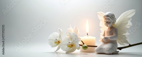 An angel statue next to white orchid flowers and burning candle on white background. Still life symbolizes grief sorrow memory spiritual. A concept of condolence funeral day of the dead