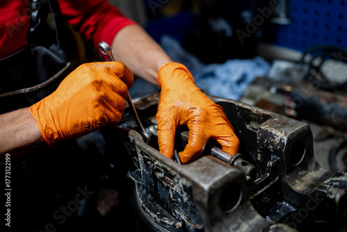 Obraz na plátně Mechanic wearing orange gloves tightening hydraulic component with wrench showin