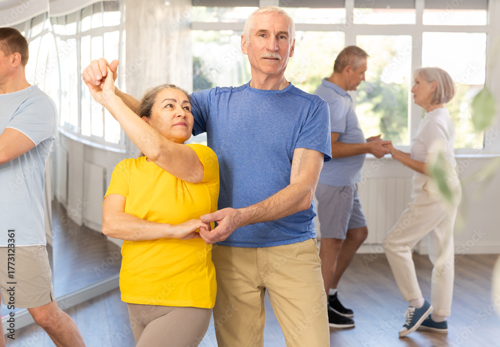 Fototapeta premium Happy smiling elderly man enjoying impassioned merengue with female partner in latin dance class. Social dancing concept..
