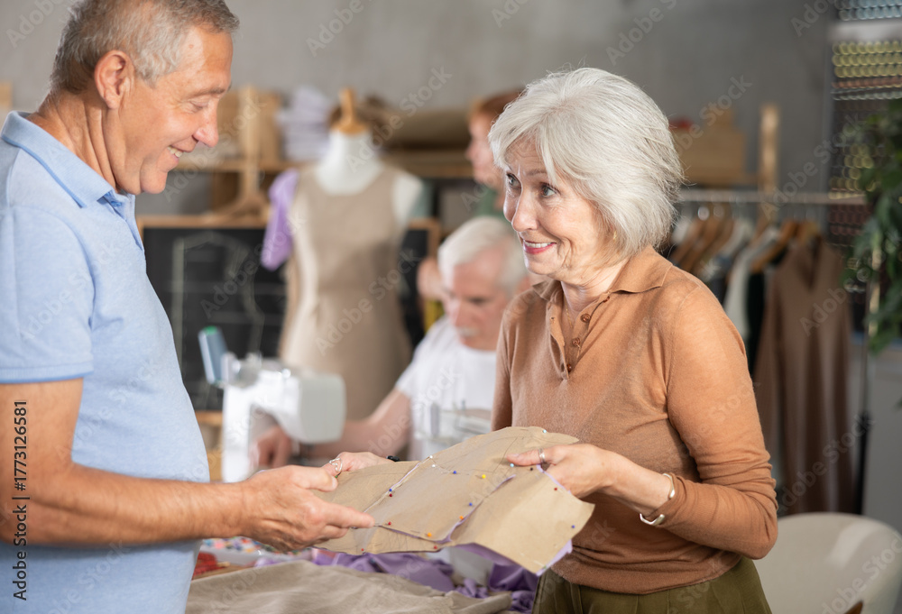 Obraz premium Elderly man and woman students discuss sewn pattern at sewing master class