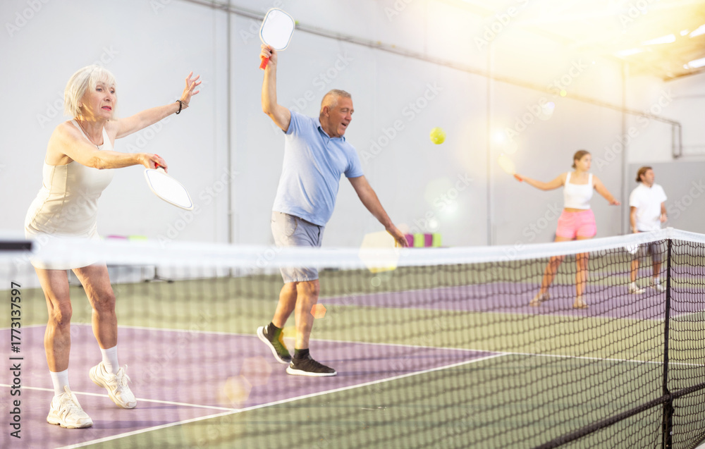 Fototapeta premium Athletic seniors playing pickleball on the court indoors